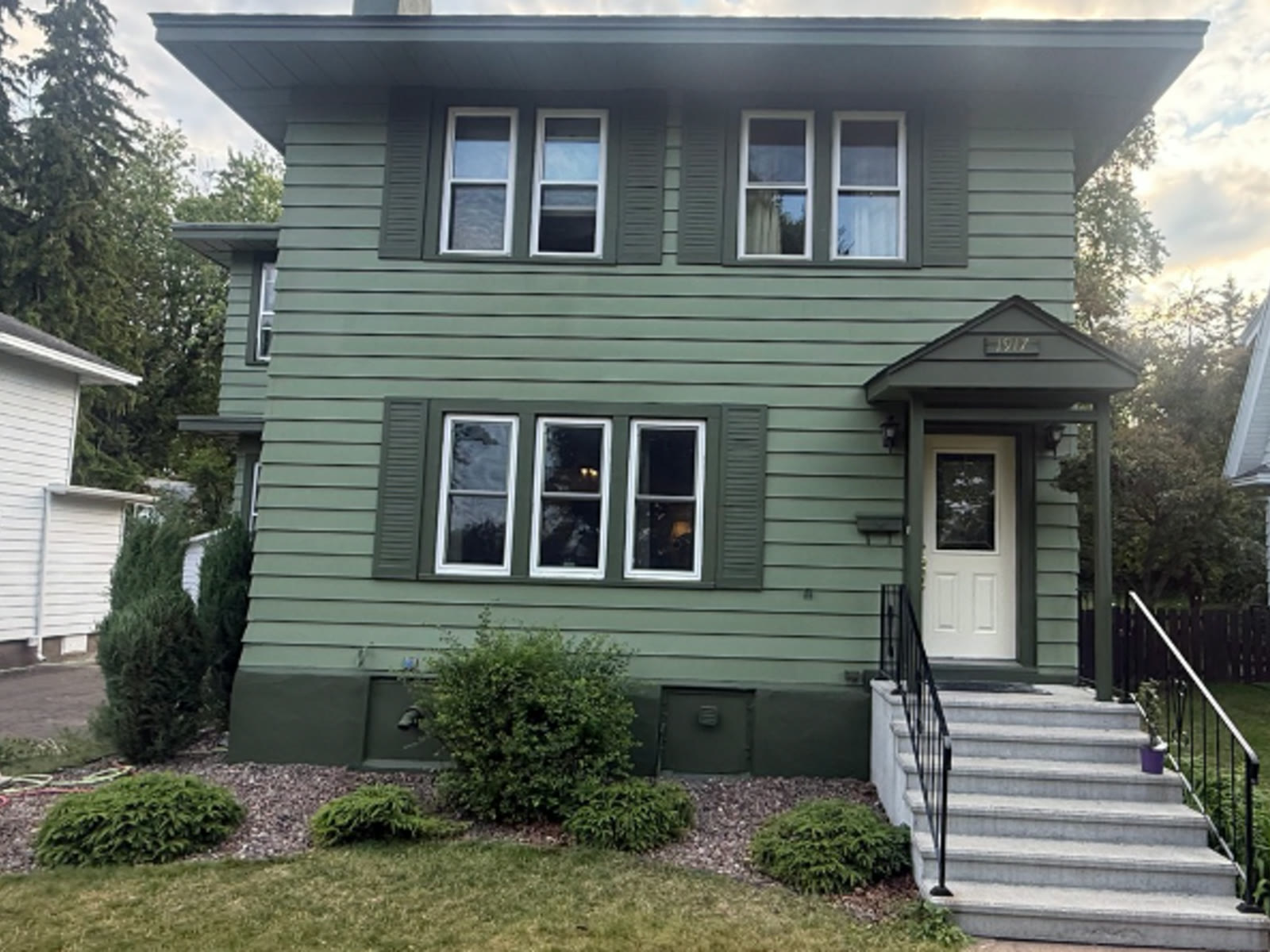 After: sage green two-story home with dark green trim and white front door